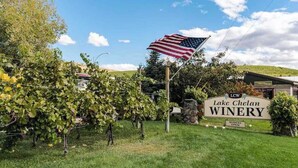 A vineyard with grapevines and an American flag, a sign for Lake Chelan Winery, and a building in the background. - Walk to Downtown 3BR Lakeview - Hot Tub - Deck (Manson)