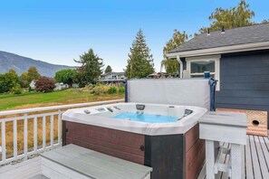 Ein Whirlpool auf einer Holzterrasse mit Blick auf ein Haus und Berge im Hintergrund.