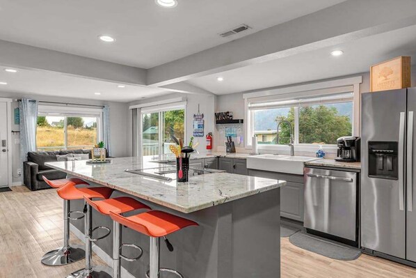 A modern kitchen with a central island, bar stools, stainless steel appliances, and large windows. - Walk to Downtown 3BR Lakeview - Hot Tub - Deck (Manson)