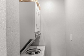 A compact laundry room with a washing machine and dryer, white walls, and a single electrical outlet. - Walk to Downtown 3BR Lakeview - Hot Tub - Deck (Manson)