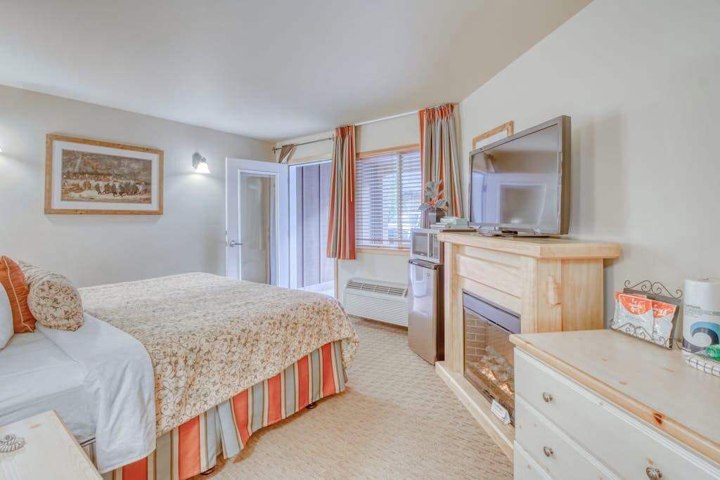 A bedroom with a bed, a television, a dresser, and a window with curtains.