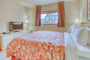 A hotel room with a bed, a television on a nightstand, a window with curtains, and a lamp on the nightstand. - Downtown 2BR Mountainview 1st-Floor - Patio (Leavenworth)