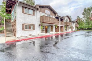 A multi-story building with balconies, a covered entrance, and a wet ground. - Downtown 2BR Mountainview 1st-Floor - Patio (Leavenworth)