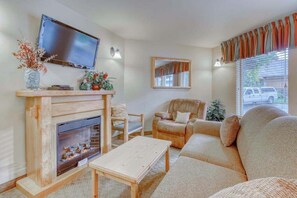 A living room with a fireplace, a television mounted above it, a sofa, a chair, and a small table. - Downtown 2BR Mountainview 1st-Floor - Patio (Leavenworth)
