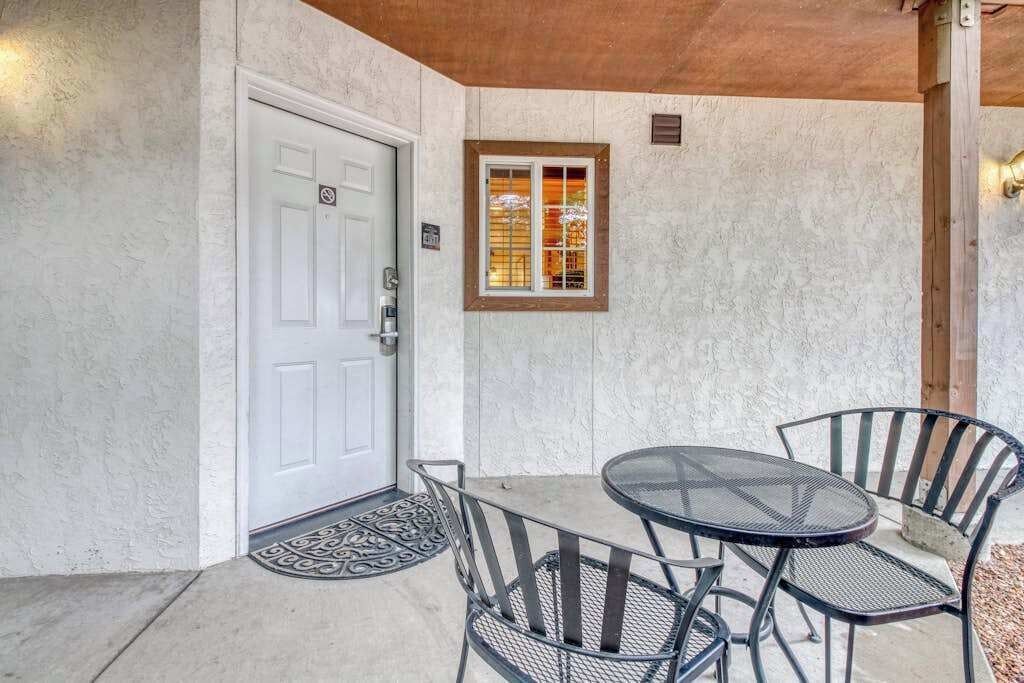 A covered patio with a table and chairs, a door, and a window with blinds.