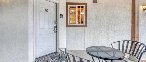 A covered patio with a table and chairs, a door, and a window with blinds.