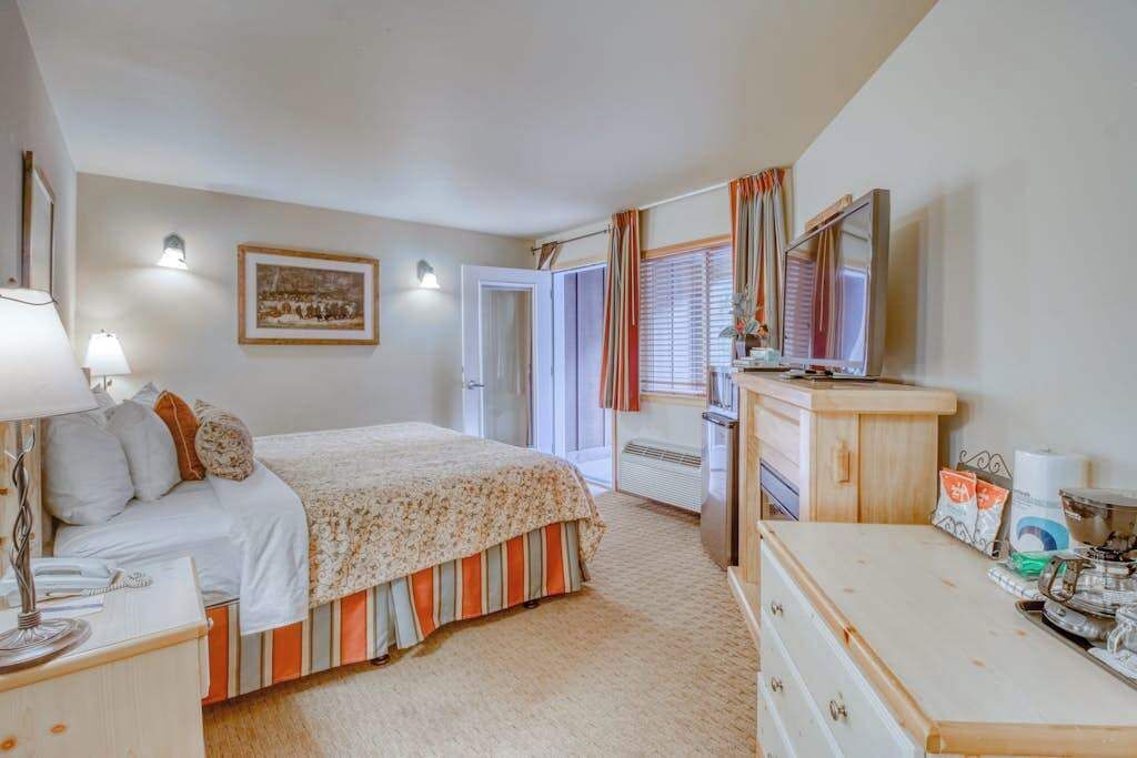 A bedroom with a bed, bedside table, lamp, dresser, and a window with curtains.