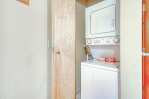 A compact laundry room with a washing machine and dryer, wooden door, and a small shelf with detergent boxes. - Downtown 2BR Mountainview 1st-Floor - Patio (Leavenworth)