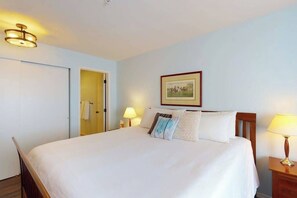 Ein Hotelzimmer mit einem Bett, Nachttischlampen, einer Tür und einem gerahmten Bild an der Wand.