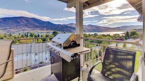 Ein Balkon mit Grill, einem Stuhl und einem schönen Blick auf Berge und einen See.