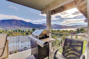 Ein Balkon mit Grill, einem Stuhl und einem schönen Blick auf Berge und einen See.