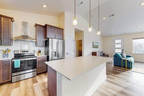 A modern kitchen with stainless steel appliances, wooden cabinets, and pendant lighting. - 3BR water view home with deck & open layout (Manson)