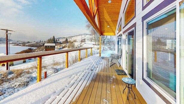 A wooden deck with a railing, overlooking a snowy landscape with a clear sky. - 3BR water view home with deck & open layout (Manson)