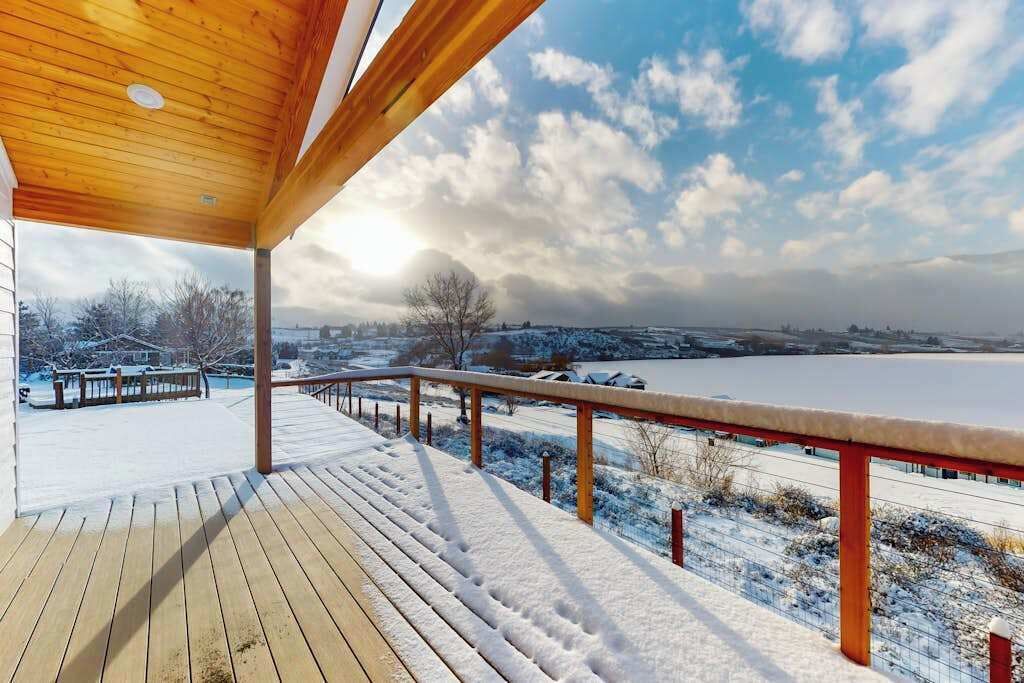 Una terraza de madera con vistas a un paisaje nevado y un cuerpo de agua.