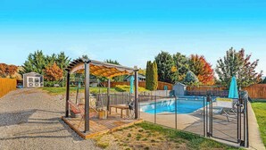 Ein Garten mit Swimmingpool, überdachter Sitzgelegenheit und einem umzäunten Spielbereich.