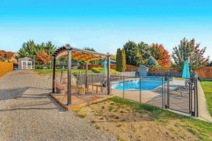 Ein Garten mit Swimmingpool, überdachter Sitzgelegenheit und einem umzäunten Spielbereich.