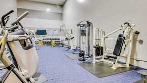 Un gimnasio con máquinas de cardio, equipo de levantamiento de pesas y una pantalla de televisión.