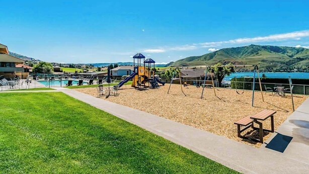 Un parque infantil con tobogán y estructuras para escalar, una piscina y vistas a colinas.