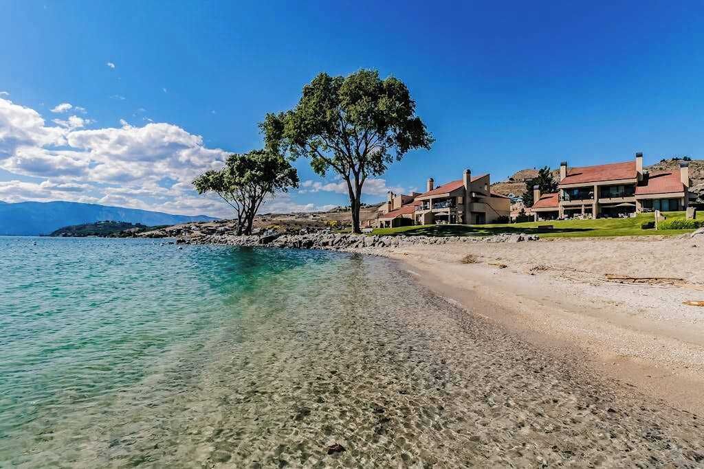 A coastal property with a clear beach, a large tree, and multiple buildings with red roofs.