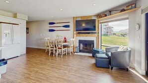 Amplia sala de estar con chimenea, una mesa de comedor con sillas y vista a una casa a través de un ventanal grande.