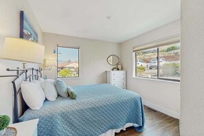 Ein Schlafzimmer mit Bett, Nachttisch, Lampe und Fenstern mit Blick ins Freie.
