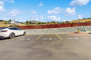 Um estacionamento com vagas demarcadas, um carro branco estacionado e uma parede vermelha ao fundo.