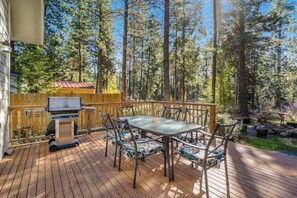 Una terraza con mesa y sillas, una parrilla y vistas a un bosque.