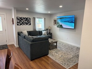A living room with a sectional sofa, a flat-screen TV, a coffee table, and a patterned rug. - Whisper Valley Villa. New Remodel. Hot Tub! Fenced back yard, High speed WiFi. (Eureka)