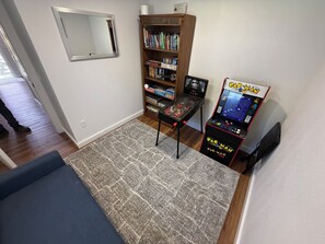 Une pièce avec une bibliothèque, une borne d’arcade Pac-Man, un miroir et un canapé bleu.