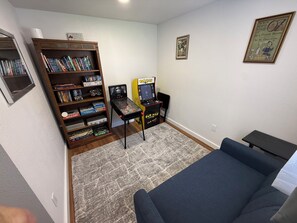 A room with a bookshelf, a Pac-Man arcade machine, a couch, and a framed picture on the wall. - Whisper Valley Villa. New Remodel. Hot Tub! Fenced back yard, High speed WiFi. (Eureka)