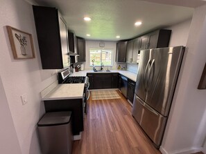 Une cuisine moderne avec des meubles de couleur sombre, des appareils électroménagers en acier inoxydable et un plancher en bois.