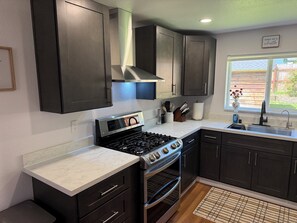 A modern kitchen with dark cabinets, a stainless steel stove, and a window with a view of the outdoors. - Whisper Valley Villa. New Remodel. Hot Tub! Fenced back yard, High speed WiFi. (Eureka)