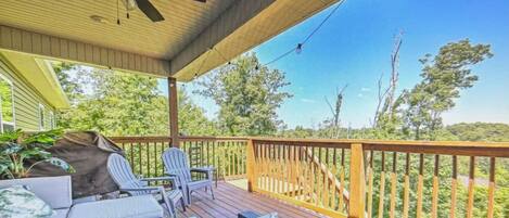 A covered outdoor deck with wicker furniture, a ceiling fan, and a view of the surrounding greenery.