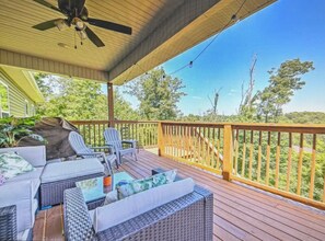Eine überdachte Terrasse im Freien mit Korbmöbeln, einem Deckenventilator und Blick auf die umliegende Bepflanzung.