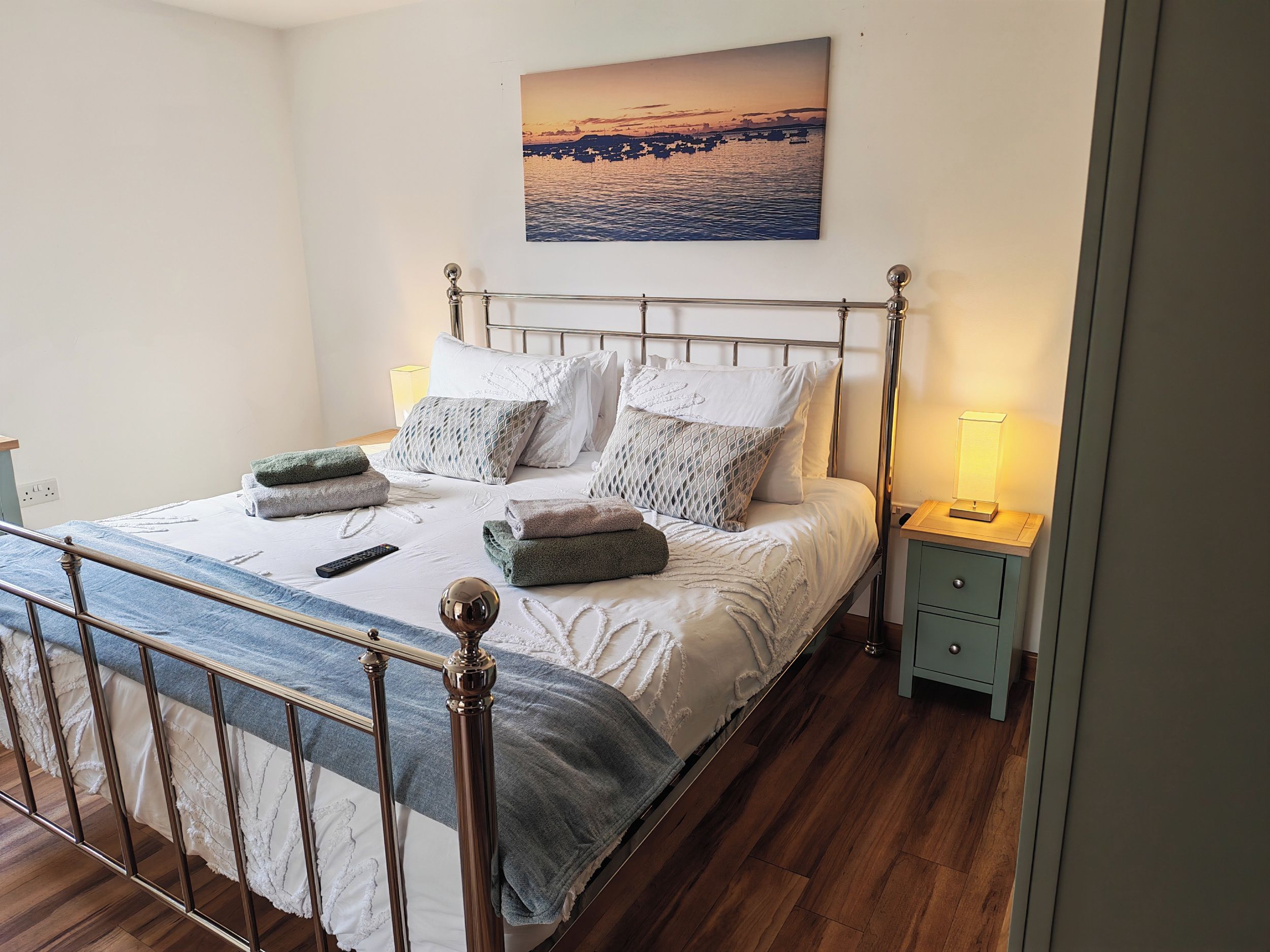 A neatly made bed with a metal frame, a bedside table with a lamp, and a wall-mounted picture.