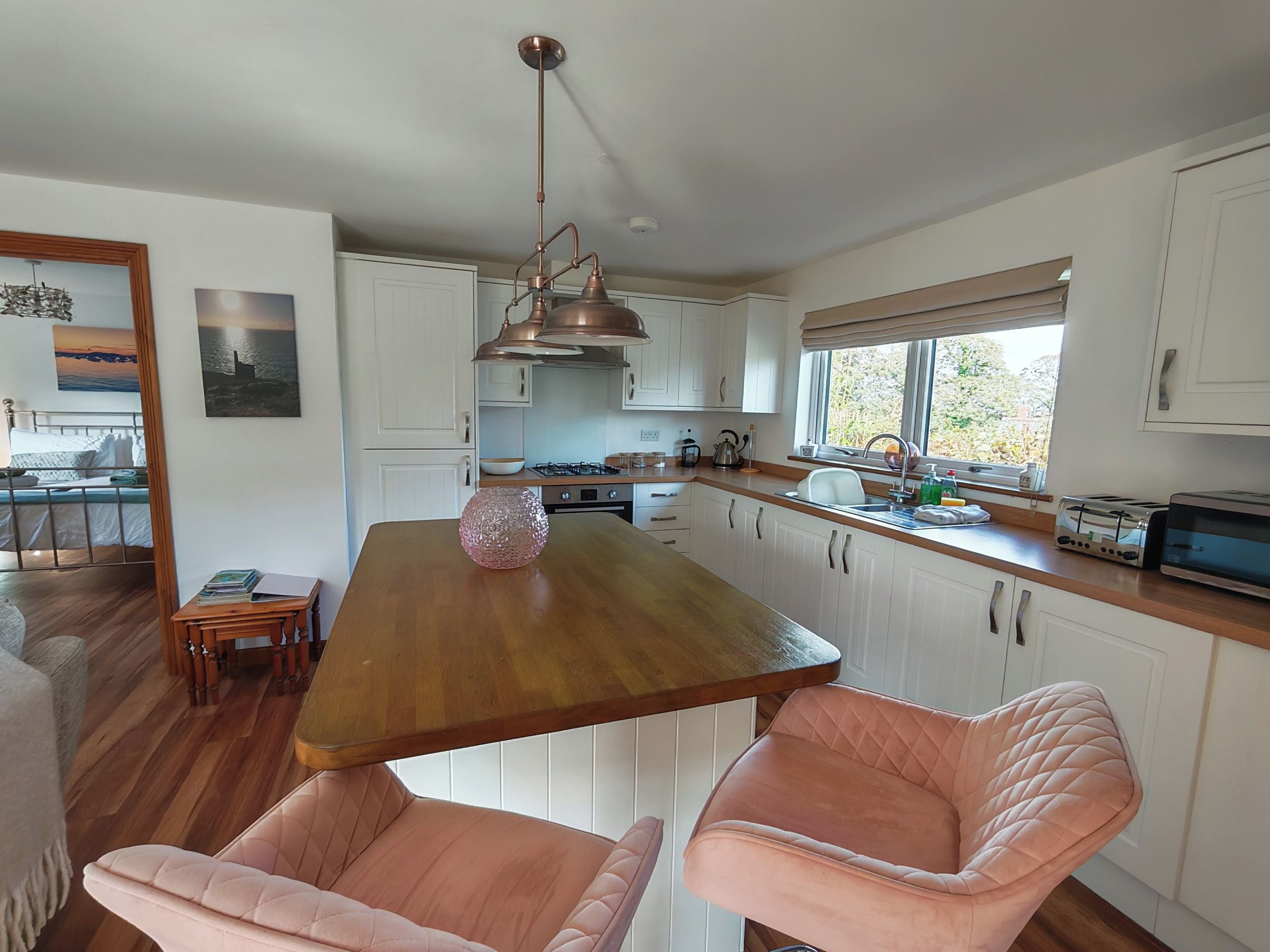Una cocina moderna con armarios blancos, una mesa de comedor de madera y dos sillas rosas.