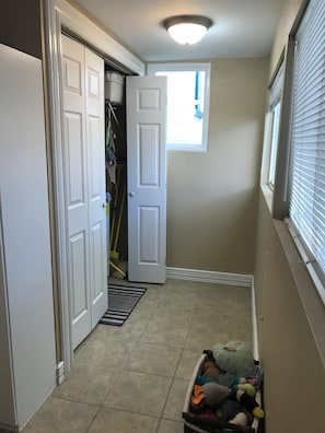 A hallway with a closed closet, a partially open door, a window with blinds, and a basket of plush toys. - Cozy 1-bedroom Victorian in quaint Platt Park with AC for relaxing stays (Denver)
