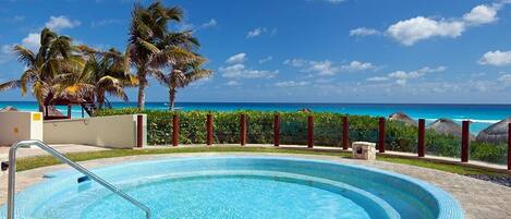 A swimming pool with a view of the ocean, surrounded by palm trees and a clear sky.