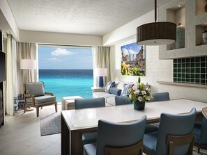 A hotel room with a dining area, a sofa set, a large window with a view of the ocean, and a decorative wall piece. - Cancun One Bedroom Villa Westin Lagunamar Resort (Cancún)