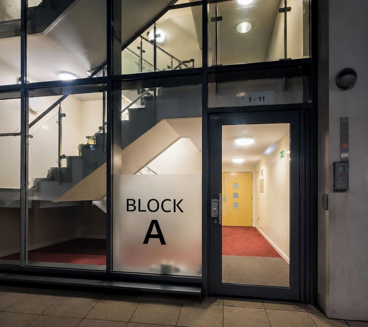 Ein Hotel Eingang mit einer Glastür, auf der 'BLOCK A' steht, und einer Innentreppe.