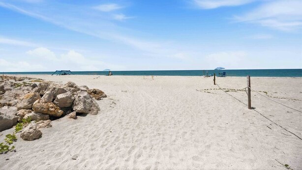 A sandy beach with a clear sky, a few umbrellas, and a rocky area on the left. - Pirate's Paradise | Manasota Key Beach Condo | Dock & Pool (Englewood)