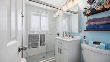 Casa de banho com cabine de duche em vidro, lavatório branco, espelho e porta-toalhas com toalhas.