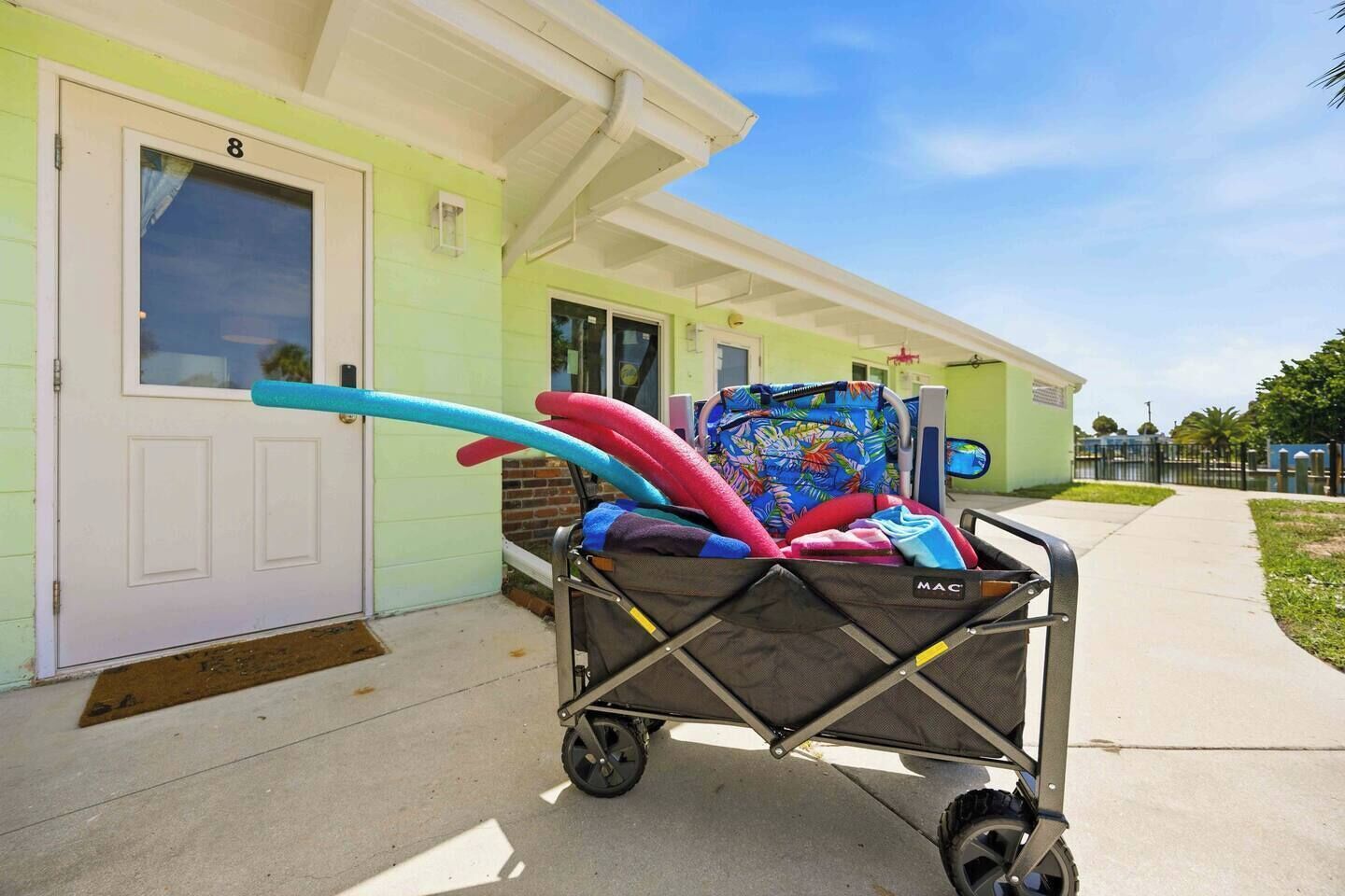 A stroller with a colorful cover parked in front of a building with a green door and a number '8' on it.