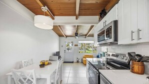 A modern kitchen with white cabinetry, a dining area with a white table and chairs, and a view of the outdoors through a door. - Pirate's Paradise | Manasota Key Beach Condo | Dock & Pool (Englewood)