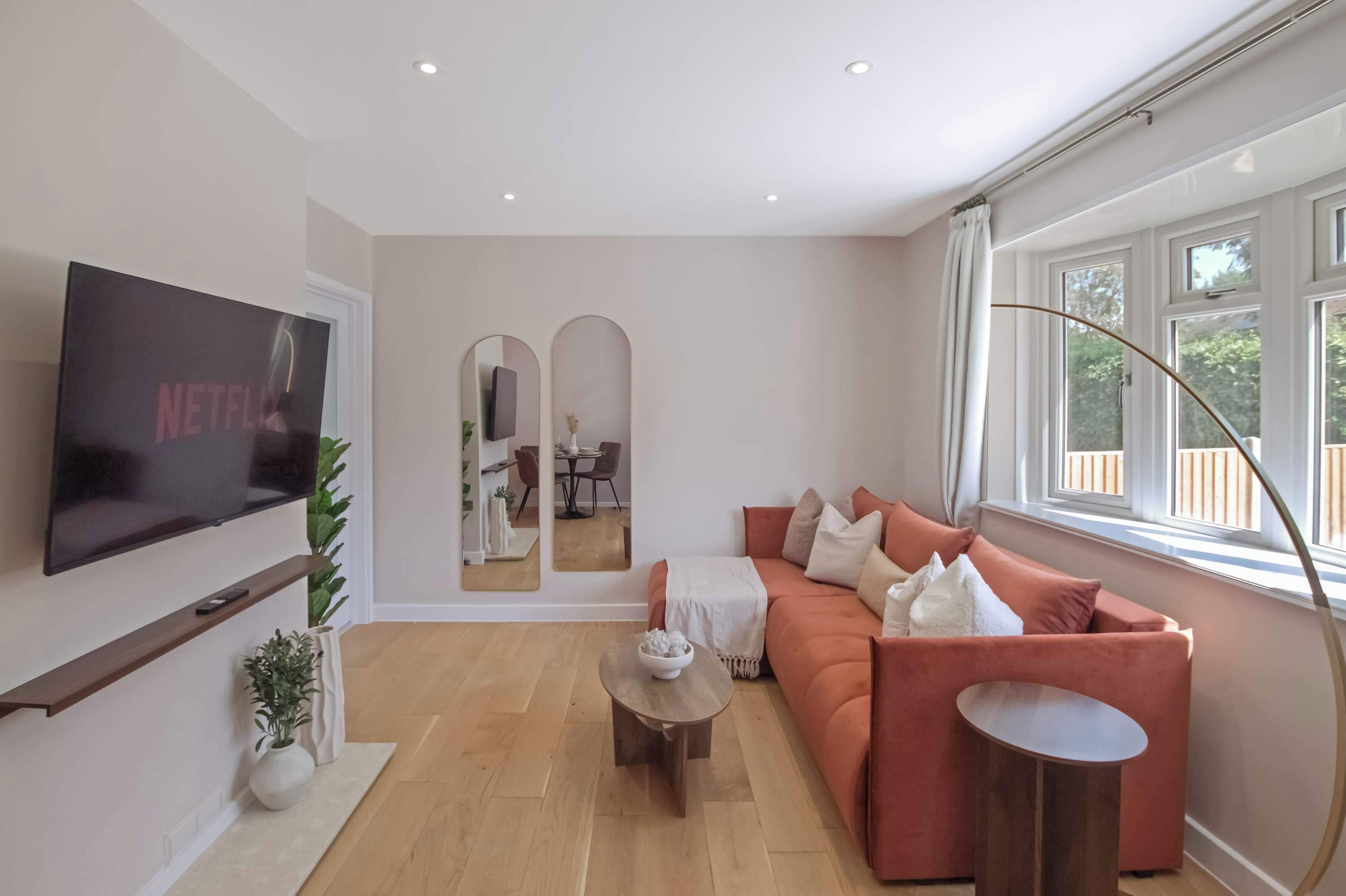Un salon moderne avec un canapé, une table basse, un téléviseur fixé au mur et une grande fenêtre.