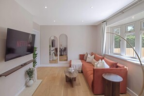 Un salon moderne avec un canapé, une table basse, un téléviseur fixé au mur et une grande fenêtre.