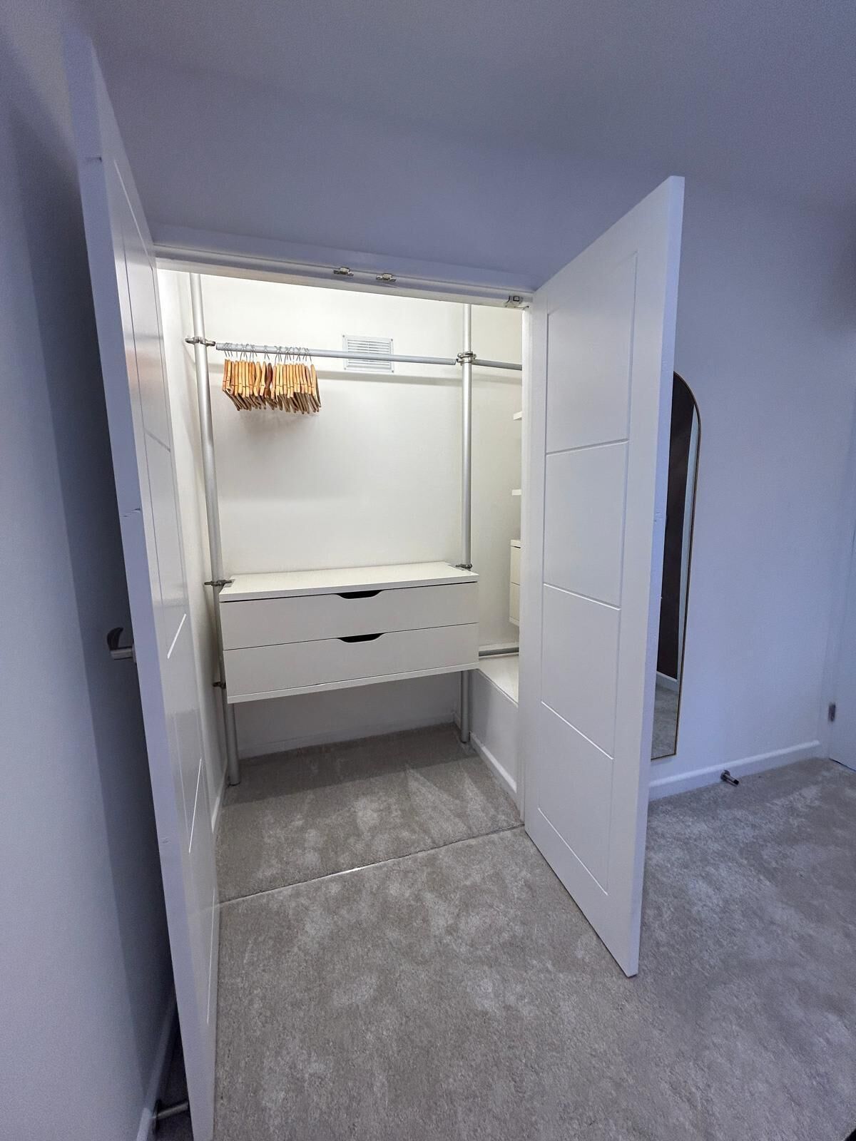 A walk-in closet with a mirrored closet door, a hanging rod, and a storage bench.