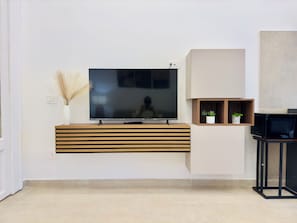 A modern living room with a flat-screen TV mounted on a wooden console, a small shelf with plants, and a black speaker on a stand. - Nova Plebiscito (Napoli)
