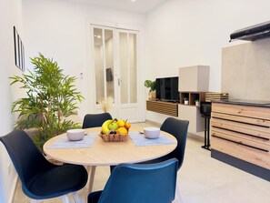 Un comedor moderno con una mesa redonda, sillas, una cesta de fruta y un televisor montado en la pared.