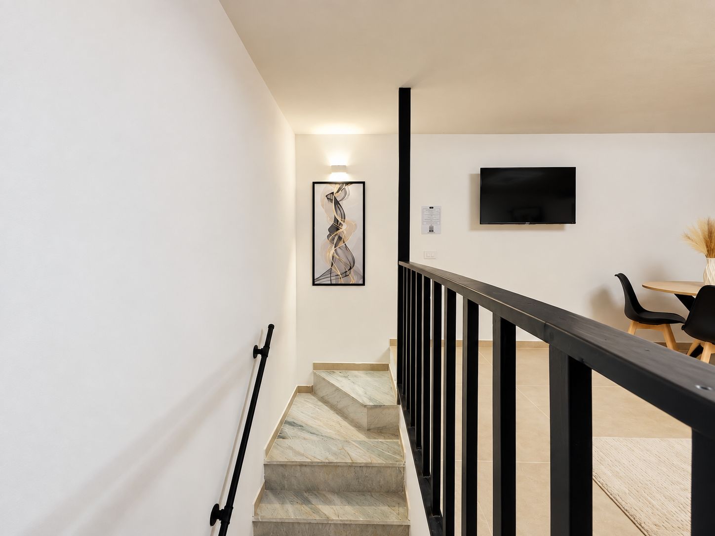 Una escalera con barandilla, un televisor de pantalla plana montado en la pared y un comedor con sillas y mesa.